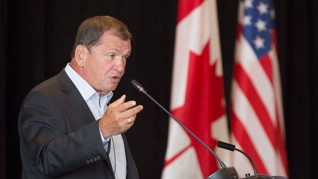 Frank McKenna, deputy chair of the TD Bank Group and former New Brunswick Premier, addresses a luncheon at a meeting of New England governors and Eastern Canadian premiers in Charlottetown on Monday, Aug. 28, 2017. A man wearing a suit jacket and dress shirt speaking into a microphone at a podium. A Canadian and United States flag hang in the background.