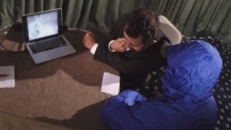 A photographer known only as "Caesar," wearing the blue hood, is in hiding, fearing for the safety of himself and his family. He agreed to speak to CBC's The Fifth Estate through a translator, so long as his identity would remain anonymous. Caesar
