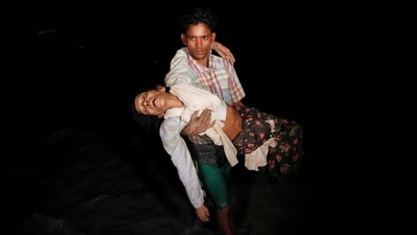 Nobi Hossain wades through the water carrying his elderly relative Sona Banu as hundreds of Rohingya refugees arrive under the cover of darkness by wooden boats from Myanmar to the shore of Shah Porir Dwip, in Teknaf, near Cox's Bazar in Bangladesh, September 27, 2017. Picture taken September 27, 2017. MYANMAR-ROHINGYA/BANGLADESH