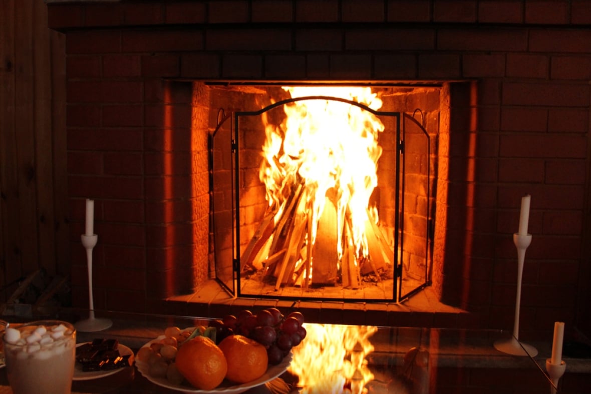 A burning fireplace near a fruit plate and a hot chocolate.