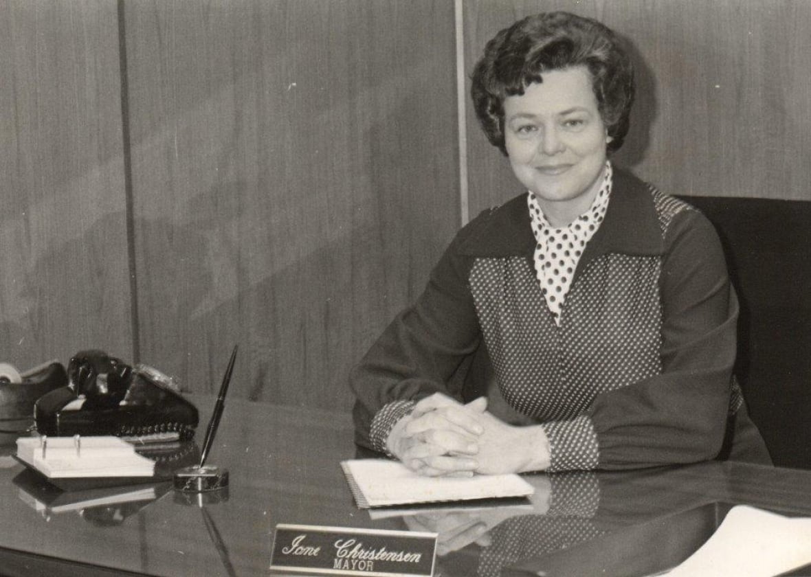 A black and white photo of a woman sitting behind a desk.