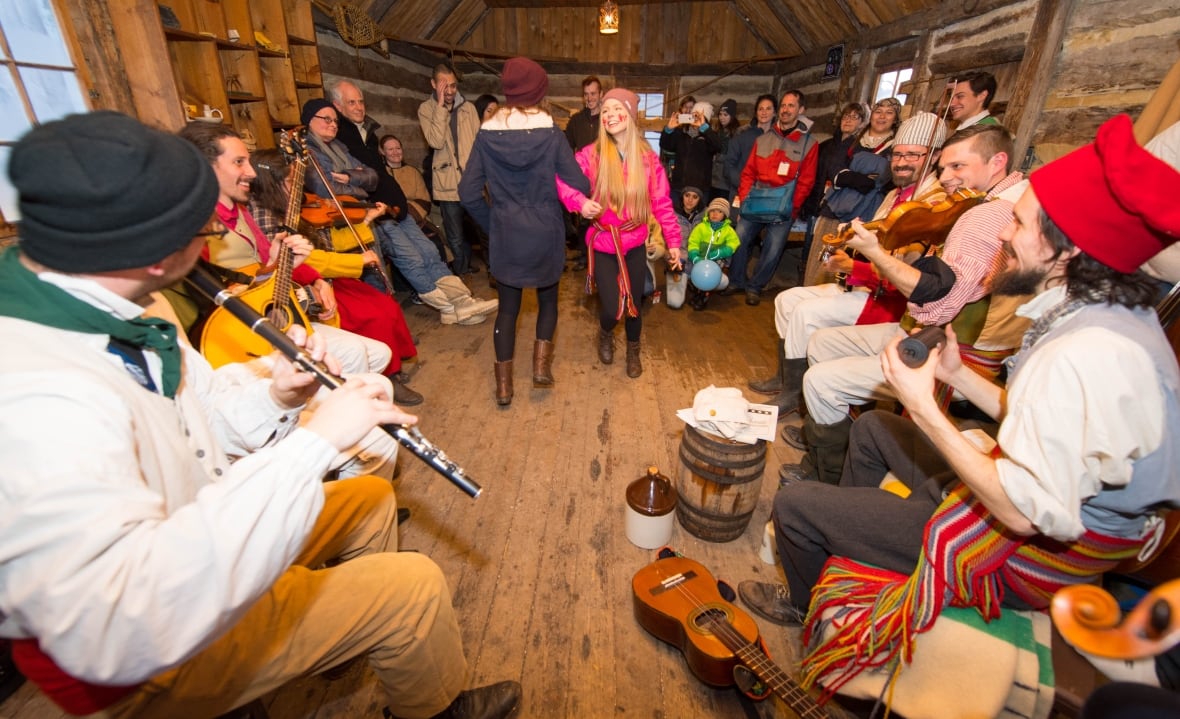 People play instruments and dance in a log cabin.