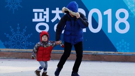 A man shields his face while towing a child against gusty winds at the Olympic Park at the 2018 Winter Olympics in Gangneung, South Korea. Gusts forced organizers to shut down the common areas in Olympic Park asking spectators to seek shelter in buildings. strong-winds-021418