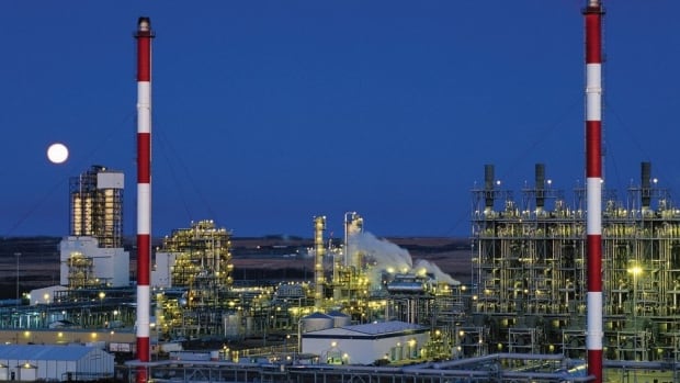 A chemical plant is shown at dusk with a full moon behind it.
