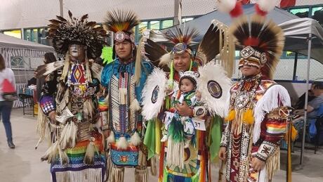 Kyrie Crookedneck is held by the dancers who performed with him during his initiation dance. Makwa Sahgaiehcan powwow baby dancer