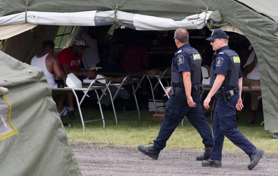 CBSA officers walk by a tent housing asylum seekers.