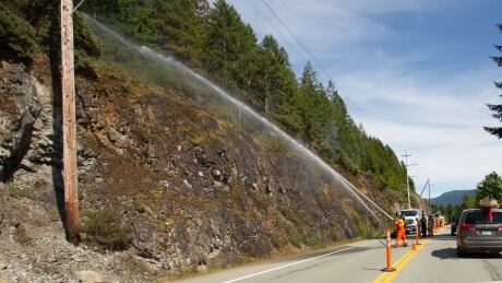 A fire fighter sprays brush on the side of Highway 4 outside of Port Alberni on Saturday July 21, 2018. Highway 4 Port Alberni Sproat Lake fire