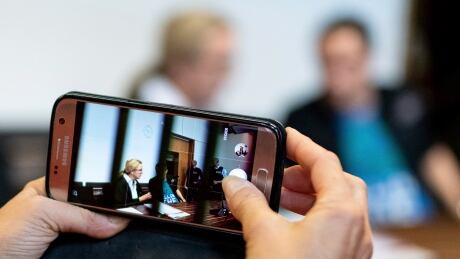 A woman takes a photo of a man in the dock of the court in Freiburg, southern Germany, on Tuesday, Aug. 7, 2018. A German mother and her partner were convicted over the repeated rape of the woman's young son and for selling him for sex on the internet. Germany Child Abuse