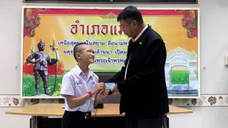 In this release by Chiang Rai Public Relations Office, Mongkol Boonpiam, left, receives an identity card denoting Thai citizenship during a ceremony in Mae Sai district in Chiang Rai province on Wednesday. Boompiam, along with Adul Samon and Pornchai Khamluang and coach Ekapol Chanthawon, had been stateless, their lack of citizenship not only restricting their upward mobility, but even their right to travel outside of Chiang Rai. Thailand Cave