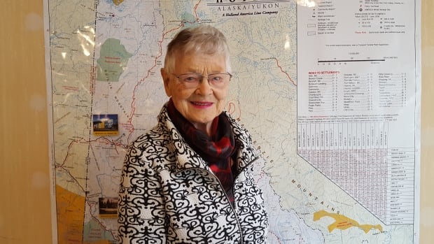 An elderly woman stands in front of a Yukon map.