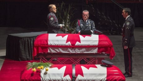 Members of the Fredericton Police Force place medals, hat and ceremonial belt on the casket for Const. Robb Costello at the regimental funeral for Costello and Const. Sara Burns, killed in the line of duty. regimental funeral