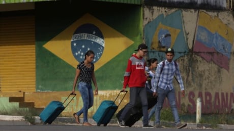FILE - In this March 9, 2018 file photo, young Venezuelans pull their luggage after crossing the border to Pacaraima, Roraima state, Brazil. One of the main border crossings between Brazil and Venezuela has reopened Tuesday, Aug. 7, after a legal fight that kept it shuttered it for nearly a day. It's part of a tug-of-war between a state government overwhelmed by hundreds of Venezuelans arriving every day and the federal government and higher courts, which insist the border must stay open. Brazil Venezuela Border
