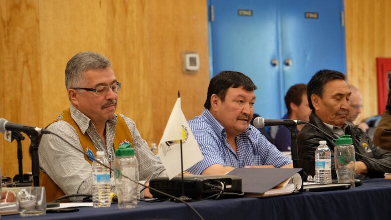 Three men sit at a table.