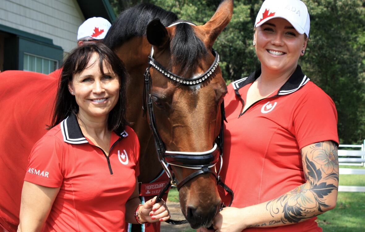 Two women stand on either side of a brown horse with black male and forelock.