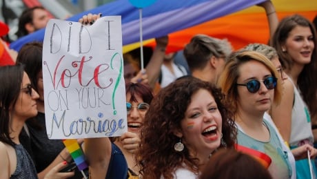 Participants, one holding a banner that reads "Did I vote on your marriage?" react, during a gay pride parade in Bucharest, Romania, Saturday, June 9, 2018. People taking part in the gay pride parade in the Romanian capital demanded more rights and acceptance for same-sex couples. Romania Gay Pride