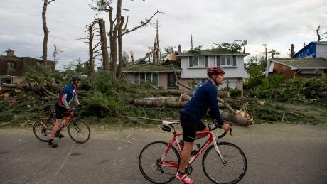 People cycle past homes damaged by trees by a tornado in the Arlington Woods neighbourhood of Ottawa, on Sunday, Sept. 23, 2018. WEA Tornado 20180923