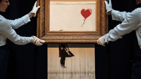 LONDON, ENGLAND - OCTOBER 12: Sotheby's employees pose with 'Love is in the Bin' by British artist Banksy during a media preview at Sotheby's auction house on October 12, 2018 in London, United Kingdom. During Sotheby's Contemporary Art Sale on 5th October the Banksy artwork 'Girl with Balloon' shredded through the bottom of the frame as it was sold. With Banksy being responsible for the shredding, the buyer has agreed to proceed with the sale and it is now titled 'Love is in the Bin' and said to be worth more than the £1.04million paid. jwt_20181012_sothebysbanksy_004.jpg