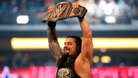 FILE - In this April 3, 2016, file photo, Roman Reigns holds up the championship belt after defeating Triple H during WrestleMania 32 at AT&T Stadium in Arlington, Texas. WWE wrestler Reigns says he will step away from the ring because he has leukemia. The 33-year-old Reigns, whose real name is Joe Anoa'i, made the announcement Monday, Oct. 22, 2018, to open the episode of "Raw."(Jae S. Lee/The Dallas Morning News via AP, File) Reigns Leukemia Wrestling