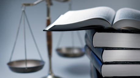 A stack of law books stands in front of a justice scale that is slightly out of focus. On top of the stack is an open law book. 690153060