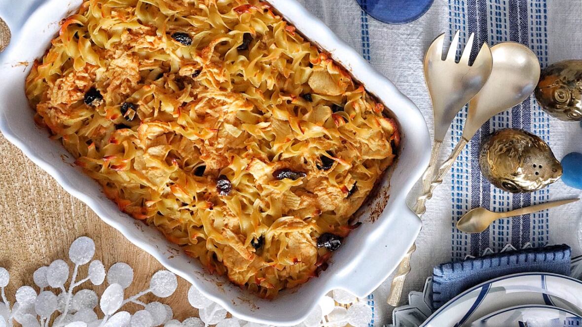 Overhead shot of a white, rectangular serving dish with a noodle kugel. The decor on the table is blue and white. 