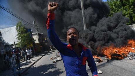 A demonstrator raises his fists, joined by other activists and opposition party members, during a protest demanding accountability from politicians for allegedly squandering billions of dollars in proceeds from Venezuelas discounted PetroCaribe oil program, in the streets of Port-au-Prince, on November 18, 2018, - Investigations by the Haitian Senate in 2016 and 2017 concluded that nearly $2 billion from a Venezuelan aid program called Petrocaribe were misused. Through Petrocaribe, Venezuela for years supplied Haiti and other Caribbean and Central American countries with oil at cut-rate prices and on easy credit terms. (Photo by HECTOR RETAMAL / AFP) (Photo credit should read HECTOR RETAMAL/AFP/Getty Images) AFP_1AY2F0