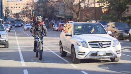 A cyclist and a vehicle ride side-by-side on the unpainted portion of the Richards Street bike lane. Cyclist car side by side