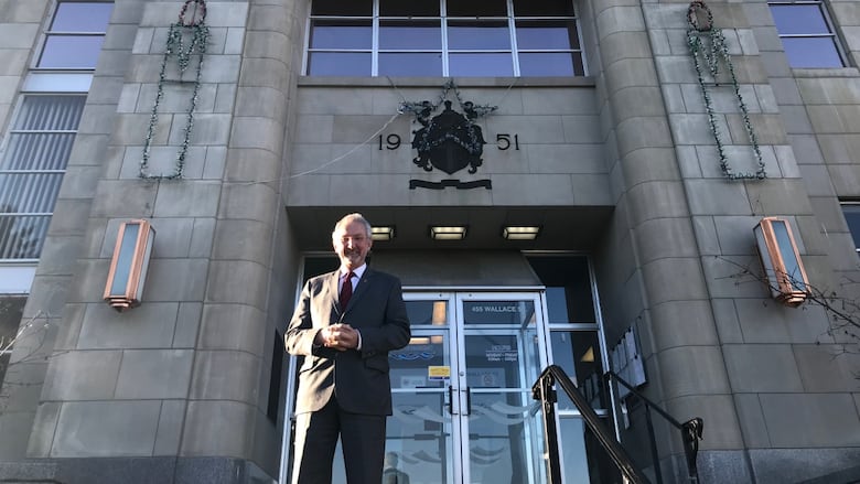 A man in a suit stands outside a stone building.
