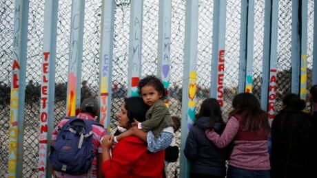 A woman carries her son as she looks at people taking part in a gathering in support of the migrant caravan in San Diego, U.S., close to the border wall between the United States and Mexico, in Tijuana, Mexico December 10, 2018. USA-IMMIGRATION/CARAVAN