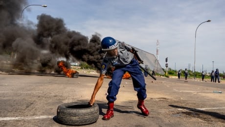 A police officer removes tyres set by protesters during a "stay-away" demonstration against the doubling of fuel prices on January 14, 2019 in Emakhandeni township, Bulawayo. - Zimbabwe's President on January 12 announced a more than 100 percent rise in the price of petrol and diesel in a move to improve supplies as the country struggles with its worst fuel shortages in a decade. In the city of Bulawayo, demonstrators attacked minibuses heading to the city centre and used burning tyres and stones to block the main routes into town. (Photo by Zinyange AUNTONY / AFP) (Photo credit should read ZINYANGE AUNTONY/AFP/Getty Images) AFP_1C79ED