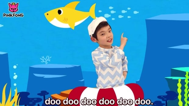 A boy with a white hat stands in front of an animated blue underwater background, singing the baby shark song