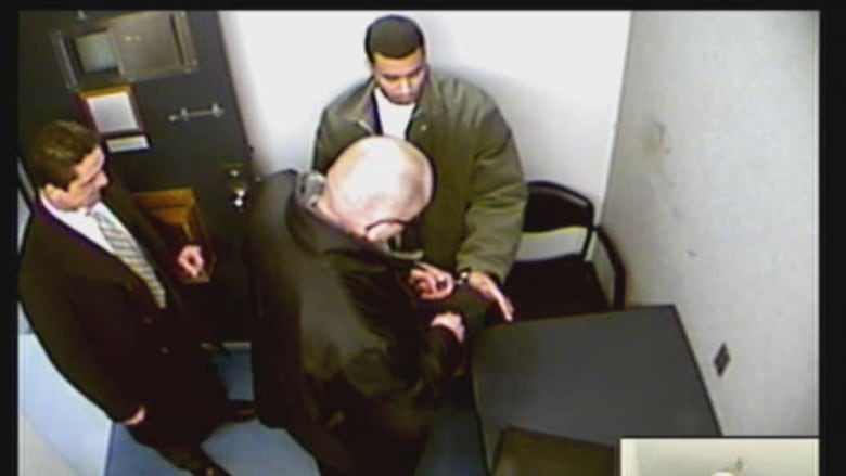 Police adjust the handcuffs of a young man.