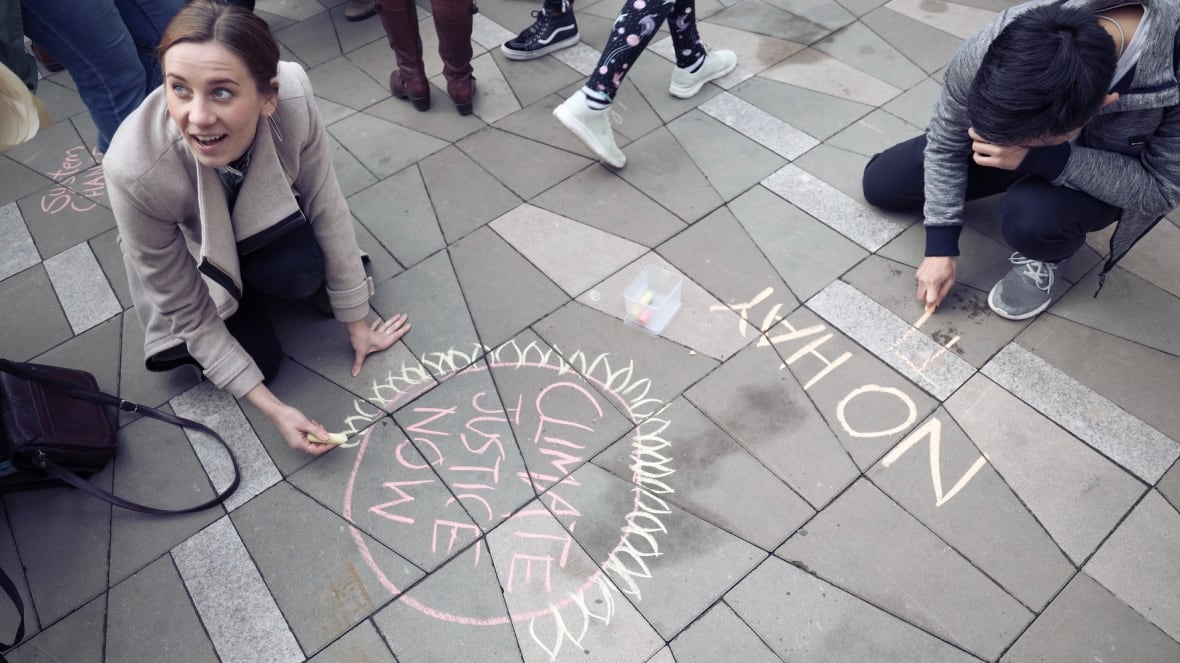 A woman writes the words "climate justice now" on a sidewalk with chalk.
