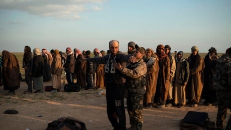 In this Feb. 22, 2019 file photo, a man is frisked by a U.S.-backed Syrian Democratic Forces (SDF) fighter after being evacuated out of the last territory held by Islamic State militants, near Baghouz, eastern Syria. The SDF fighters who drove the Islamic State from its last strongholds called Monday for an international tribunal to prosecute hundreds of foreigners who have been rounded up. Syria