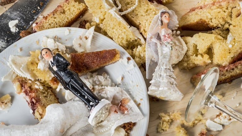 Two wedding cake toppers, models of a groom and bride, lie in the remains of a smashed wedding cake