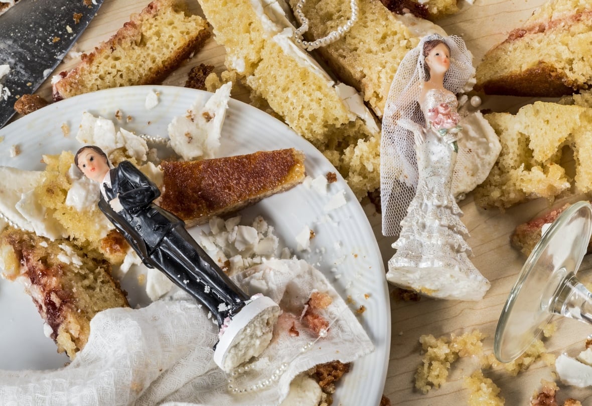 Two wedding cake toppers, models of a groom and bride, lie in the remains of a smashed wedding cake