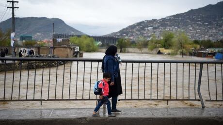 An Afghan woman with her child cross a bridge after heavy rain falls along the Kabul river in Kabul on April 16, 2019. - Torrential rainstorms have lashed drought-stricken Afghanistan in recent days, bringing widespread flooding that has killed at least five people and washed away homes including in the capital Kabul, officials said on April 16. (Photo by WAKIL KOHSAR / AFP) (Photo credit should read WAKIL KOHSAR/AFP/Getty Images) 1137494972