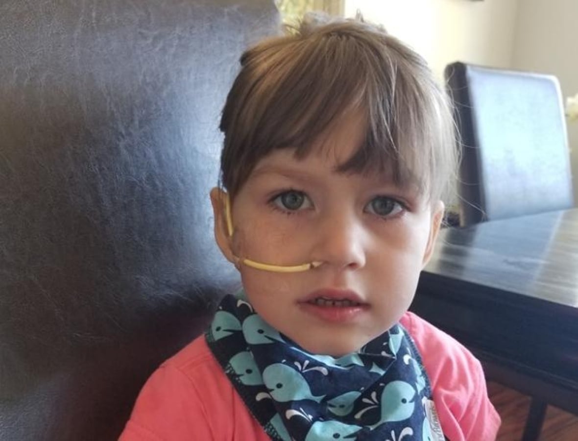A young girl with blond hair and a medical tube in her nose