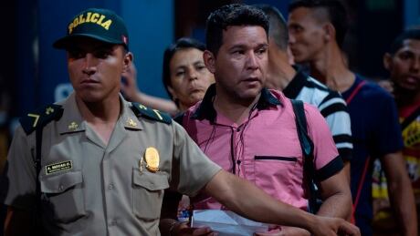 A Peruvian policeman assists Venezuelan citizens waiting in line to get a refugee application at a Peruvian border post at the binational border attention centre (CEBAF) in Tumbes on June 14, 2019. - Alleging security reasons, the Peruvian government announced last week that Venezuelans will need a humanitarian visa, as well as a passport, from June 15 to enter Peru, where there are already some 800,000 migrants from that country. 1150143371