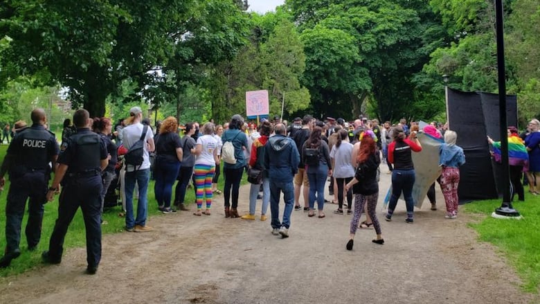 Many people gather at a park with signs as police walk by