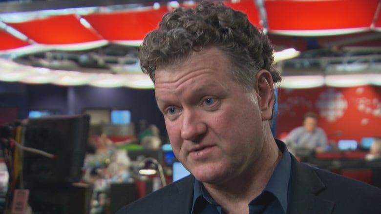 Man looks at camera in front of newsroom backdrop