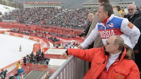 In this file photo taken Saturday, March 8, 2014, Russian President Vladimir Putin, foreground, watches downhill ski competition of the 2014 Winter Paralympics in Roza Khutor mountain district of Sochi, Russia, as Russia's sports minister Vitaly Mutko stands behind. On Tuesday, Dec. 5, 2017 IOC imposed a lifetime Olympic ban on Mutko. IOC Russian Doping