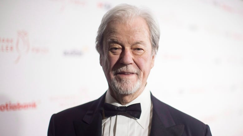 An elderly man with a tux stares into the camera