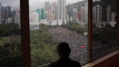 A person stands near a window overlooking a protest on Victoria Park in Hong Kong on Sunday, Aug. 18, 2019. Thousands of people streamed into a park in central Hong Kong on Sunday for what organizers hope will be a peaceful demonstration for democracy in the semi-autonomous Chinese territory. (AP Photo/Kin Cheung) APTOPIX Hong Kong Protests