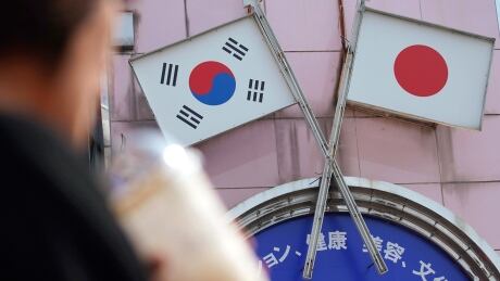 FILE - In this Aug. 2, 2019, file photo, a woman walks past an advertisement featuring Japanese and South Korean flags at a shop in Shin Okubo area in Tokyo. South Korea says it’ll nullify an intelligence-sharing pact with Japan amid bitter trade dispute with its Asian neighbor. (AP Photo/Eugene Hoshiko, File) South Korea Japan Intel Deal