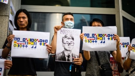 Activists holding placards - one an illustration (C) of Simon Cheng and others carrying a message using International Code of Signals (ICS) flags - gather outside the British Consulate-General building in Hong Kong on August 21, 2019, following reports that the Hong Kong consulate employee had been detained by mainland Chinese authorities on his way back to the city. - An employee of Britain's consulate in Hong Kong who went missing earlier this month is being held in China, Beijing confirmed on August 21. (Photo by Anthony WALLACE / AFP) (Photo credit should read ANTHONY WALLACE/AFP/Getty Images) 1163037403