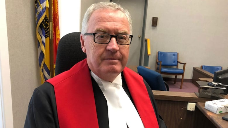 A man sitting in a courtroom wearing black and red robes. 