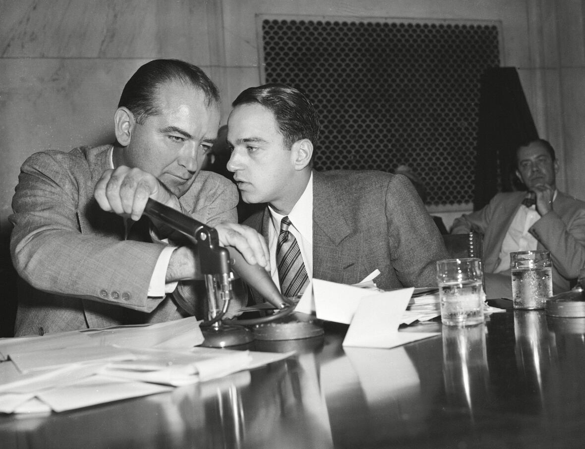 Senator Joseph McCarthy covers the microphones with his hands while having a whispered discussion with his chief counsel Roy Cohn during a committee hearing, in Washington