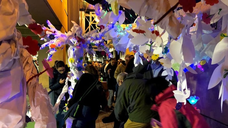 Night photo of people walking through alley with papers and coloured lights hanging above them