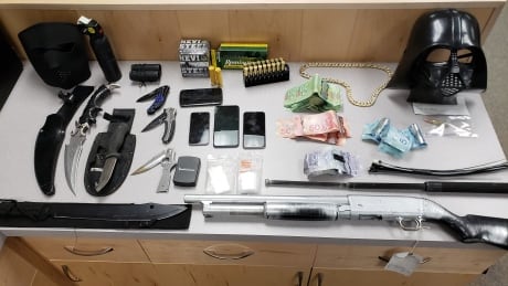 A Darth Vader mask can be seen on a table of weapons and cash seized by the RCMP on Oct. 19, 2019. Four people are now facing charges as a result of the seizure and RCMP are looking for a fifth. RCMP weapons