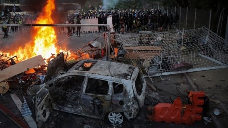 Students stand near a fire and a charred vehicle during a face-off with riot police at the Chinese University in Hong Kong, Tuesday, Nov. 12, 2019. Police fired tear gas at protesters who littered streets with bricks and disrupted morning commutes and lunch breaks Tuesday after an especially violent day in Hong Kong's five months of anti-government demonstrations. Hong Kong Protests